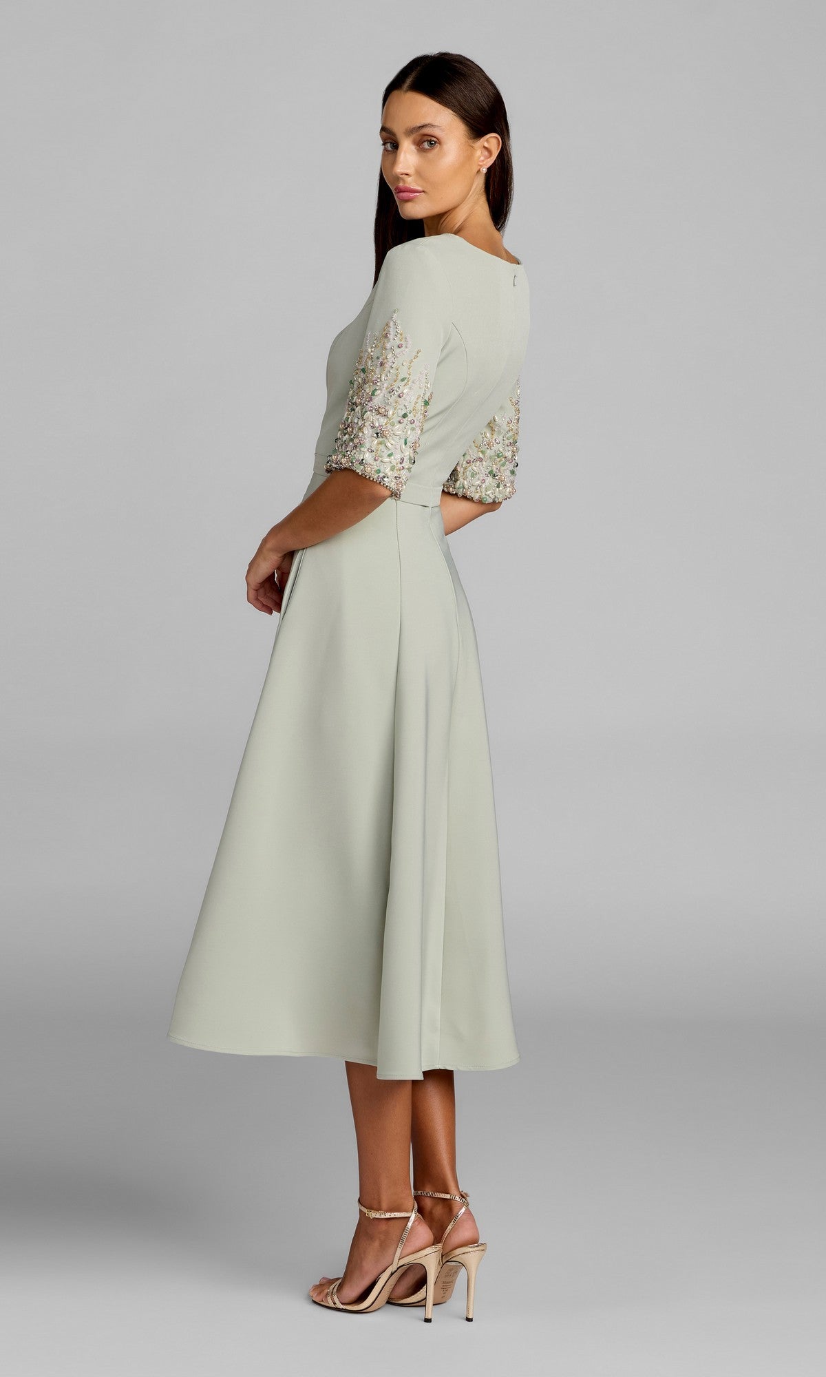 Woman standing sideways wearing the Tea-Length Party Dress: Mac Duggal 2372 in light green crepe, featuring embellished short sleeves and paired with nude heeled sandals, against a plain gray background.